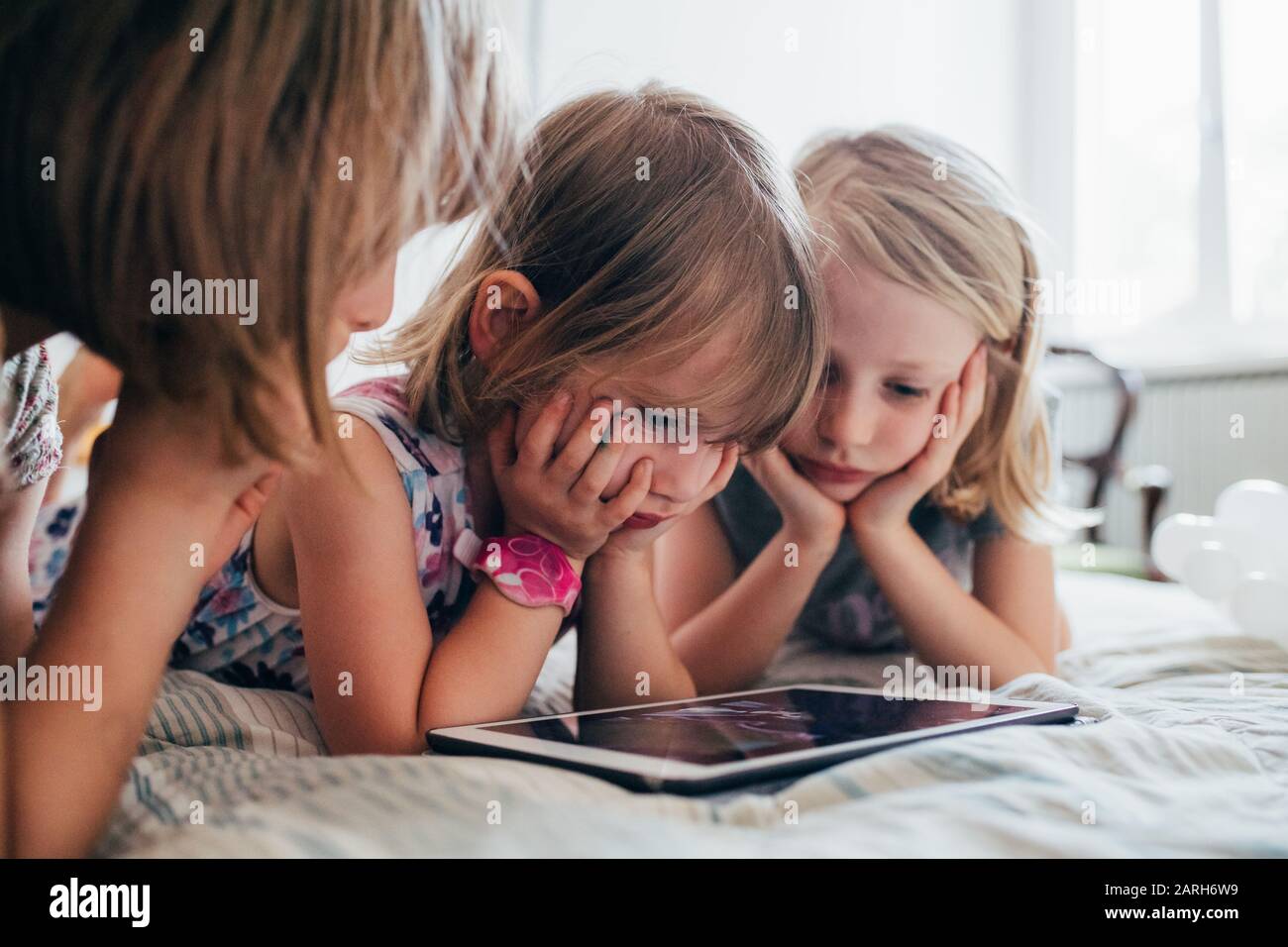 Three little sisters indoor at home using tablet lying in bed - education, technology, streaming concept Stock Photo