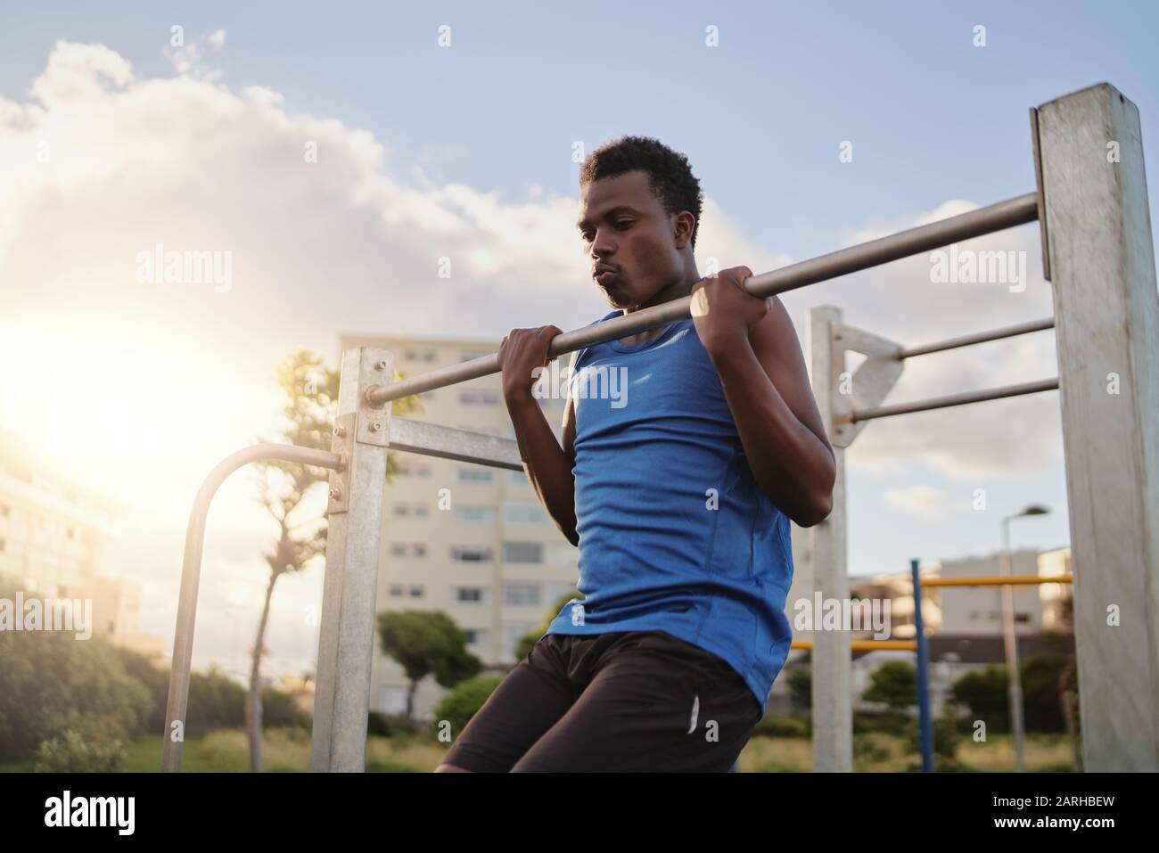 An african american young fit man doing pull ups on horizontal bar in the public park outdoors Stock Photo