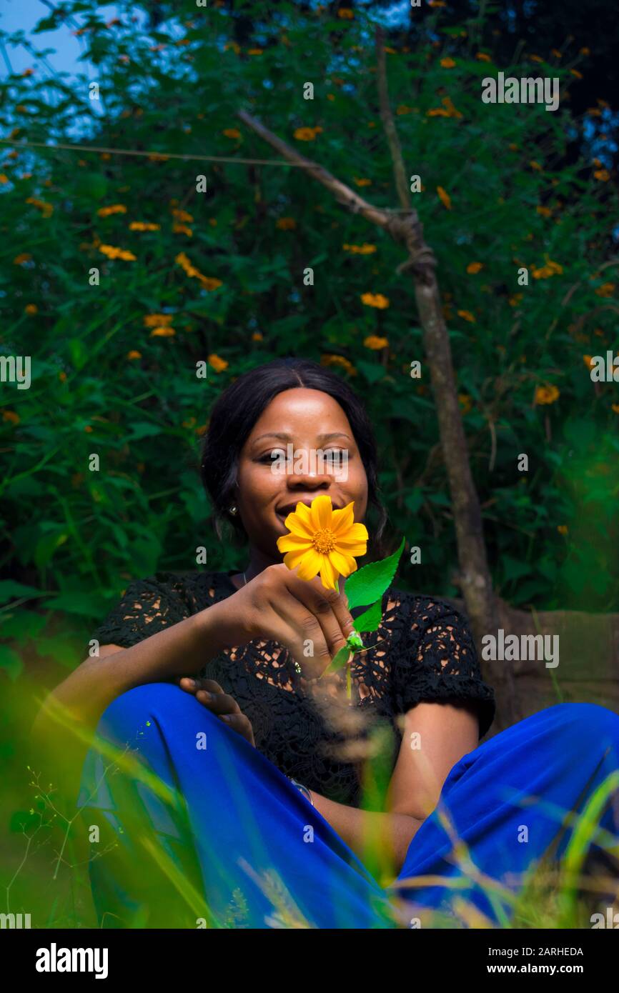 young black woman holding a tree marigold flower sitting in a garden alone Stock Photo