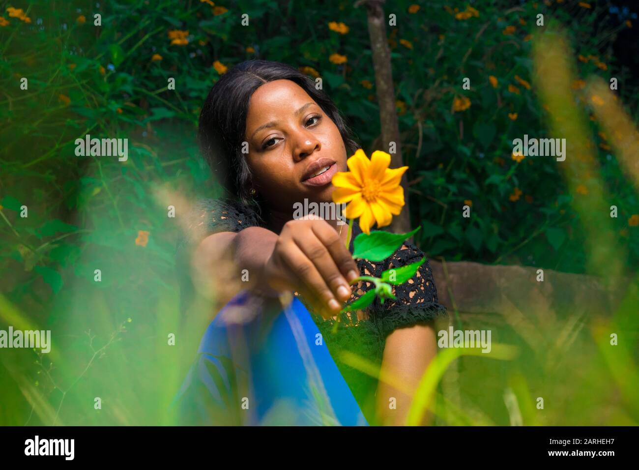 black girl holding a tree marigold sunflower sitting in a garden alone Stock Photo