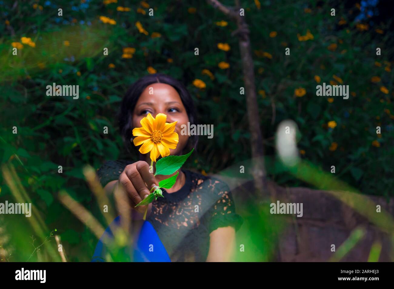 black girl holding a tree marigold flower sitting in a garden alone Stock Photo