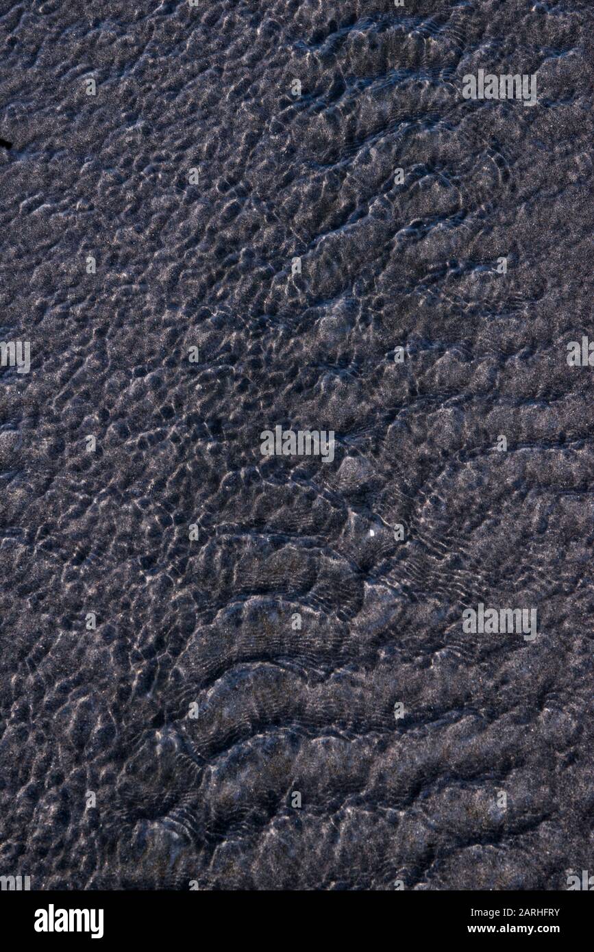 Detail of water flowing over black sand at Oakura Beach, New Zealand Stock Photo