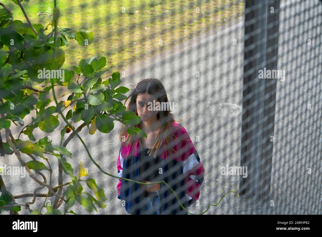 Trendy teenager walks past behind industrial mesh looking ahead. Stock Photo
