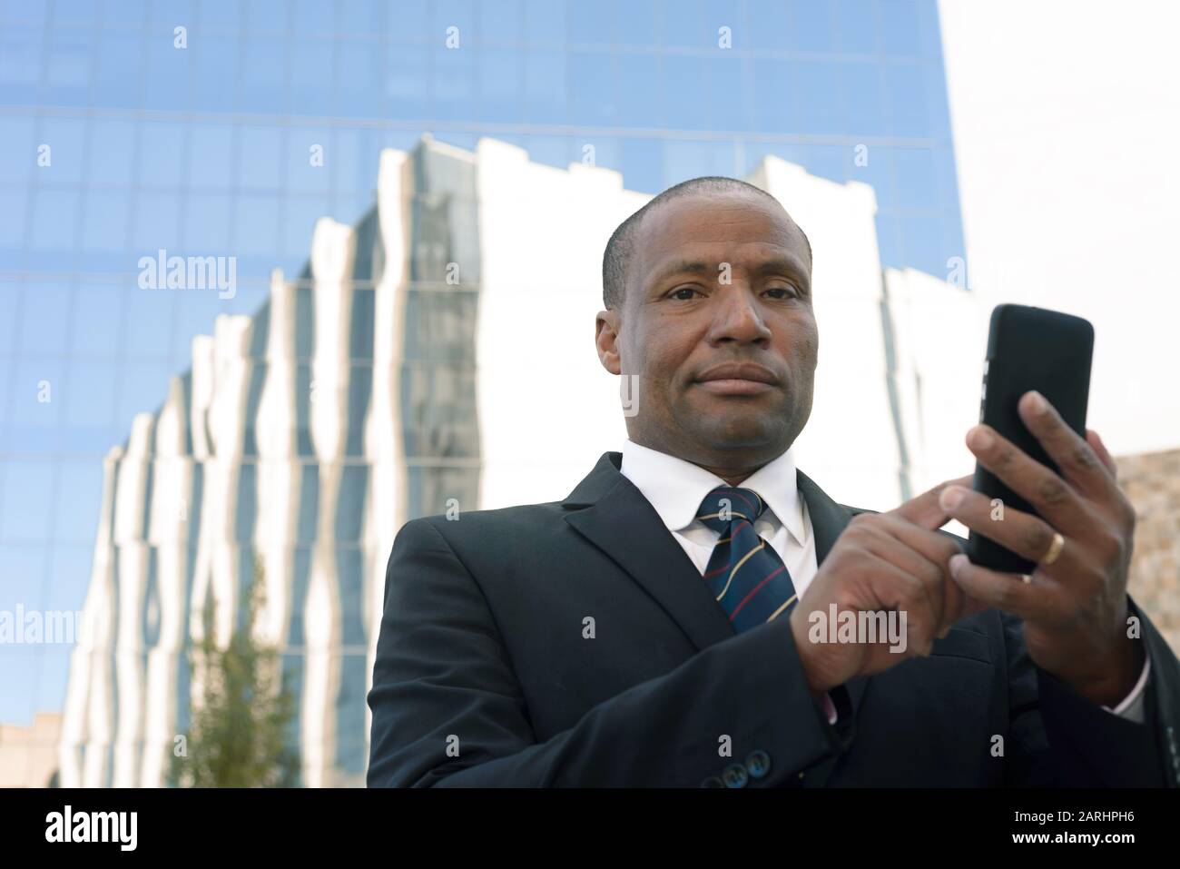 Black businessman in a suit looking successfull with a smartphone in an urban background Stock Photo