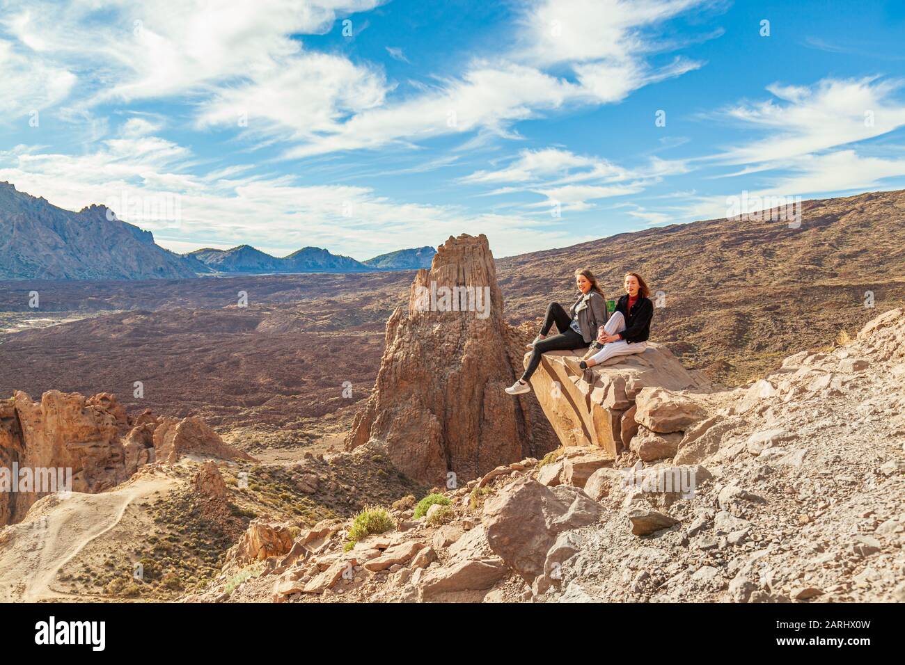 two young women sitting on rock outcrop high over teide national park tenerife Stock Photo