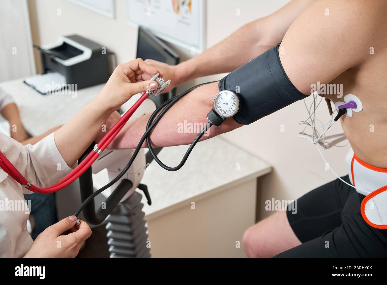 The nurse measures arterial tension. Man patient, pedaling on a bicycle ergometer stress test system for the function of heart checked. Athlete does a Stock Photo