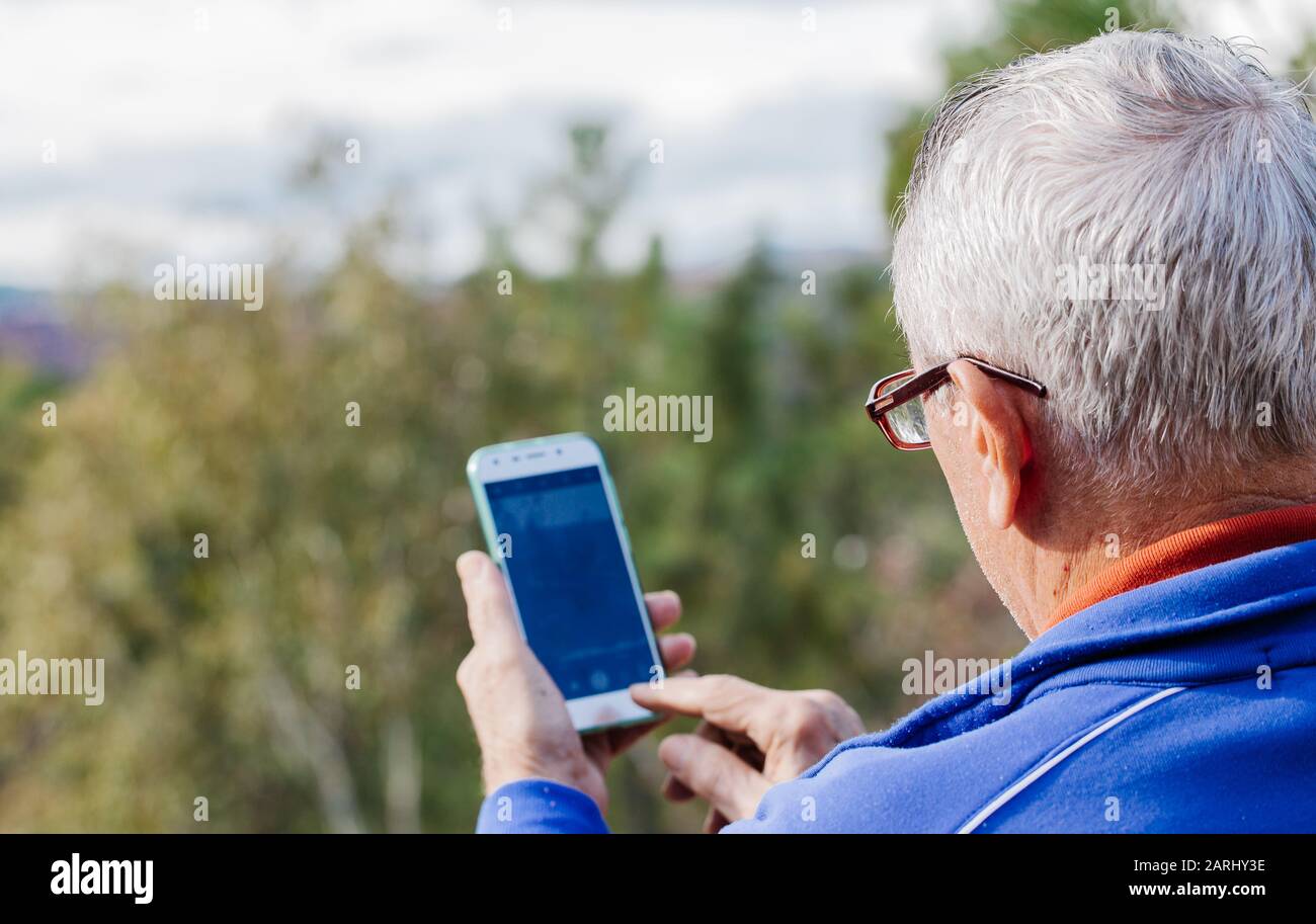 Rear view of old man with glasses taking a picture with the mobile Stock Photo