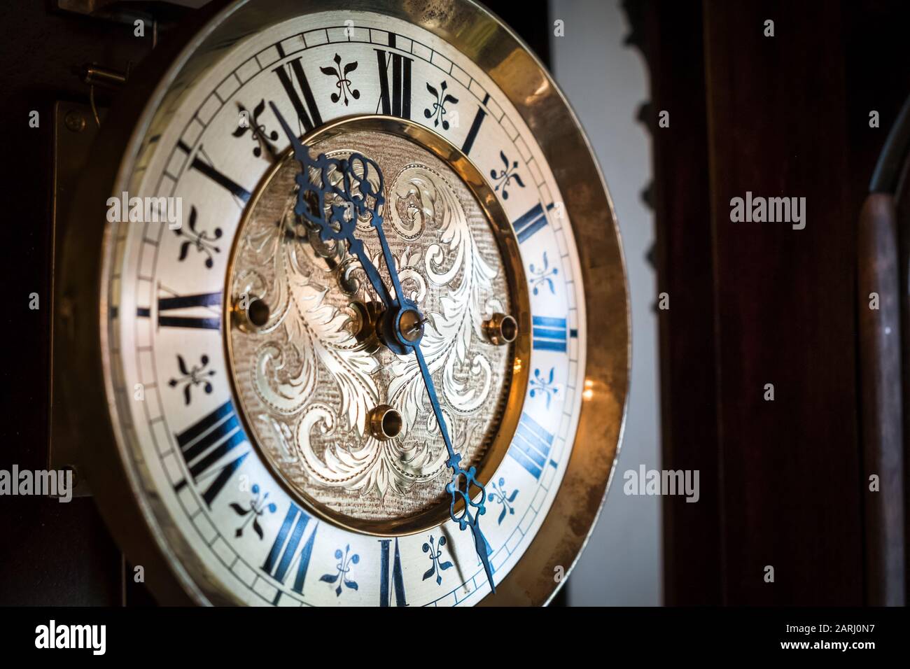A closeup of a golden wall clock dial shimmering in the morning light with Baroque floral designs engraved Stock Photo