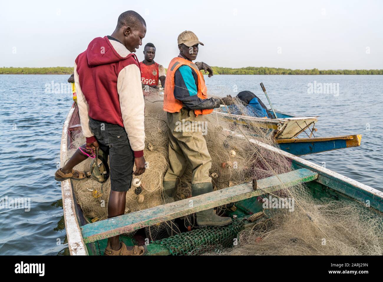Fischer mit Netz in Ihrem Boot am Flussufer, Insel Jinack Island, Gambia, Westafrika  |  fishermen with net on their boat at the river shore, Jinack I Stock Photo