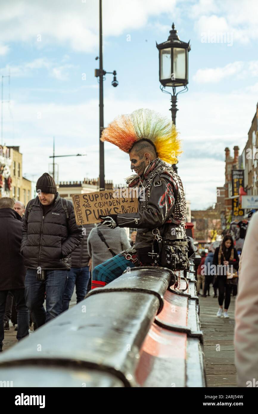 London / UK - Dec 01, 2019: tattoed face punk with colorful mohawk sitting on the street in Camden Town. The punk subculture emerged in the United Kin Stock Photo
