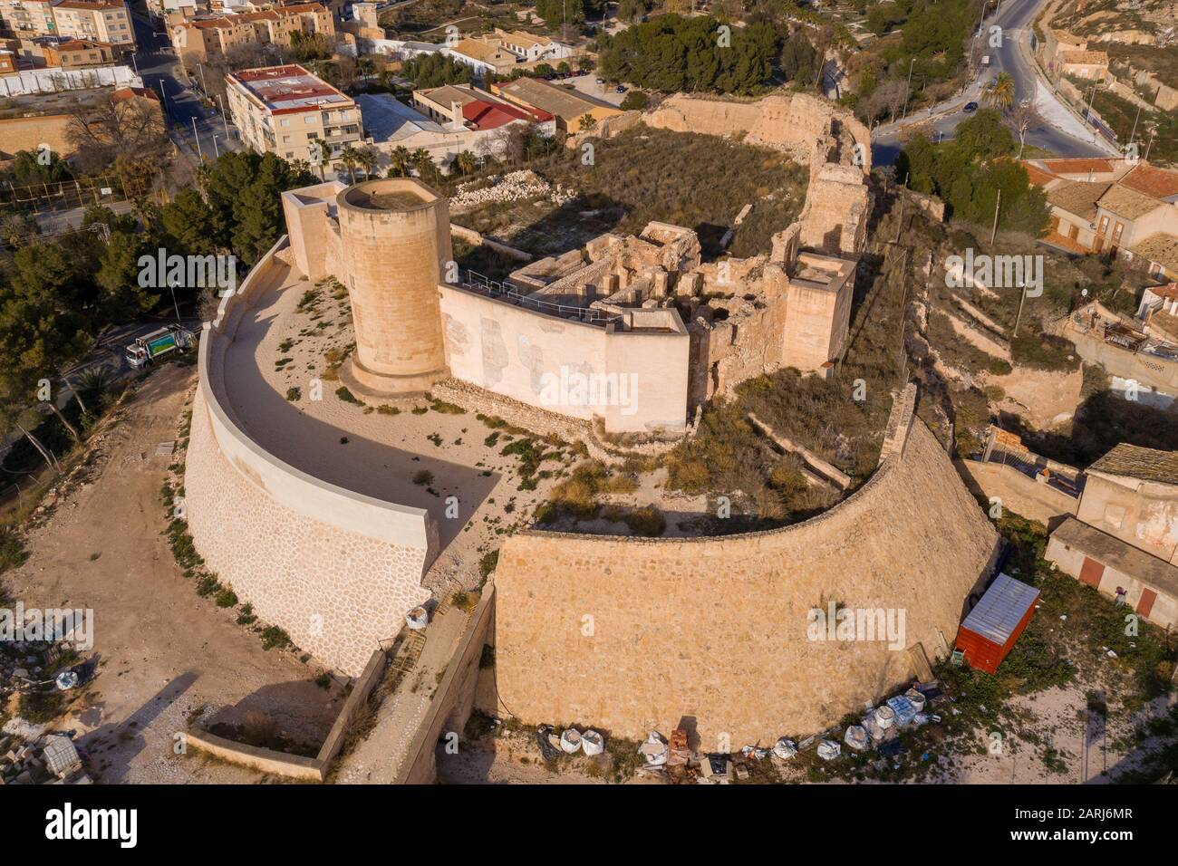 Aerial panoramic view of medieval Elda castle above the town with partially restored walls, towers and gate made of white lime stone in Spain Stock Photo