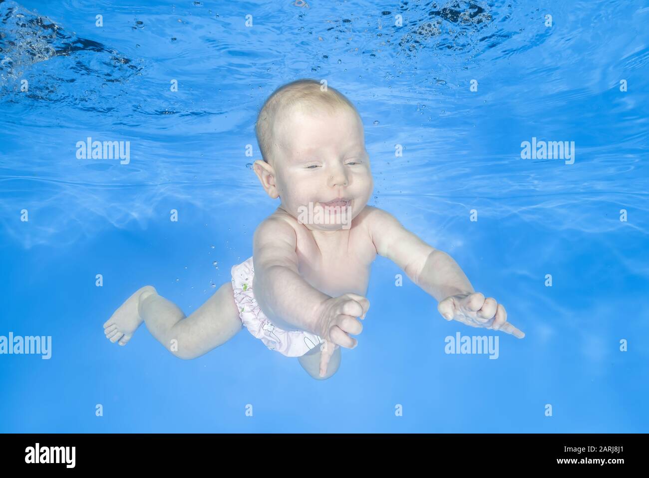 Little baby girl learns to swims underwater. Girl swimming underwater in the pool on a blue water background. Healthy family lifestyle and children wa Stock Photo