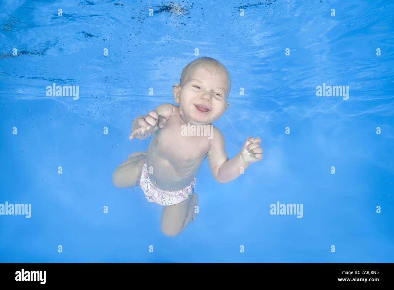 Little baby girl learns to swims underwater. Girl swimming underwater in the pool on a blue water background. Healthy family lifestyle and children wa Stock Photo