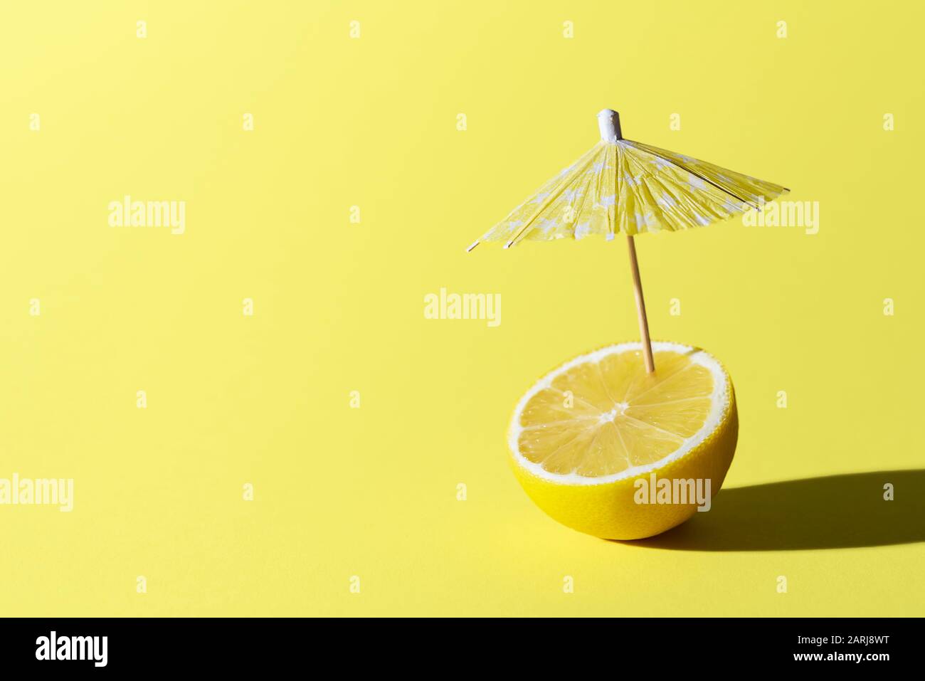 Lemon fruit and a cocktail umbrella stuck in it, on yellow background