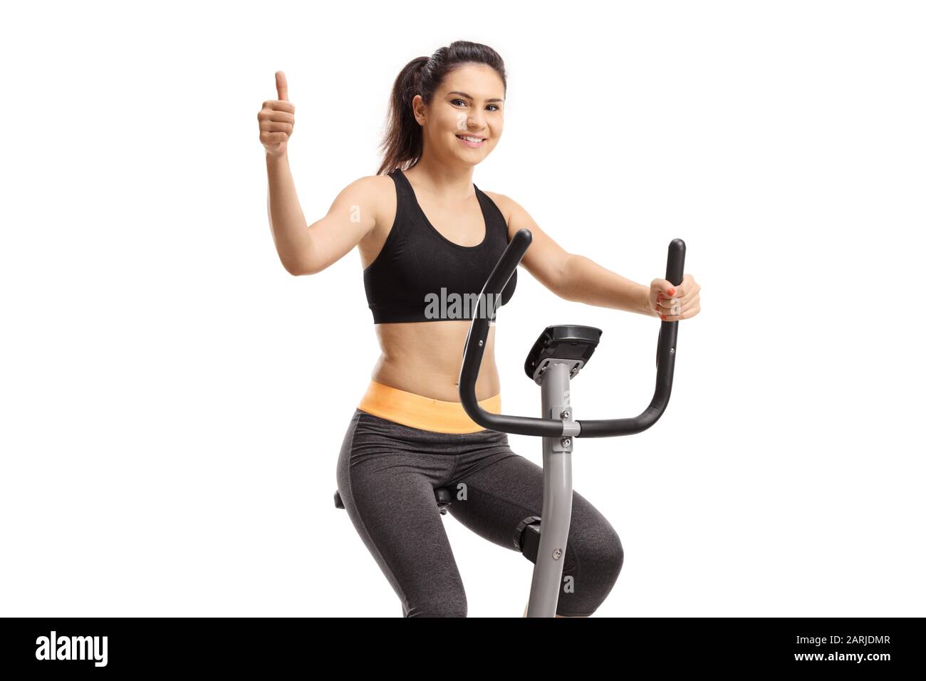Girl riding a stationary bike and showing thumb up isolated on white background Stock Photo