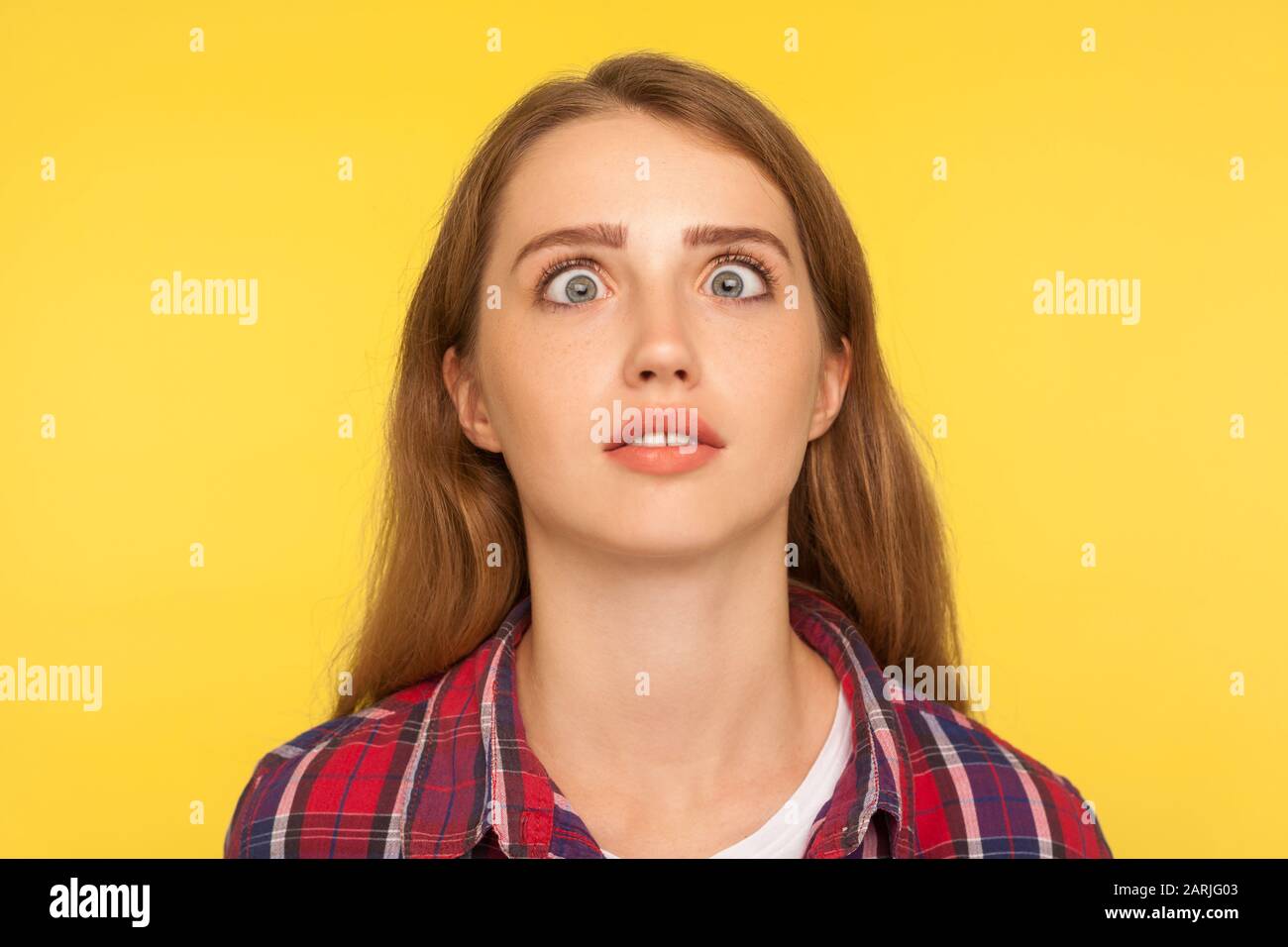 Closeup portrait of funny silly ginger woman in checkered shirt looking up cross eyed with stupid dumb face, girl has awkward confused comical express Stock Photo
