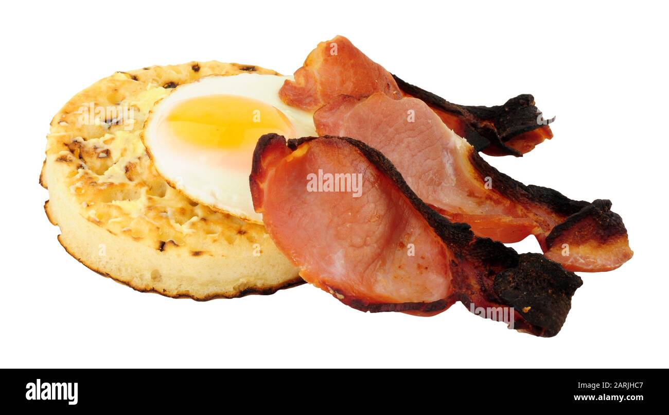 Fried egg and smoked bacon rashers on a large English crumpet isolated ...