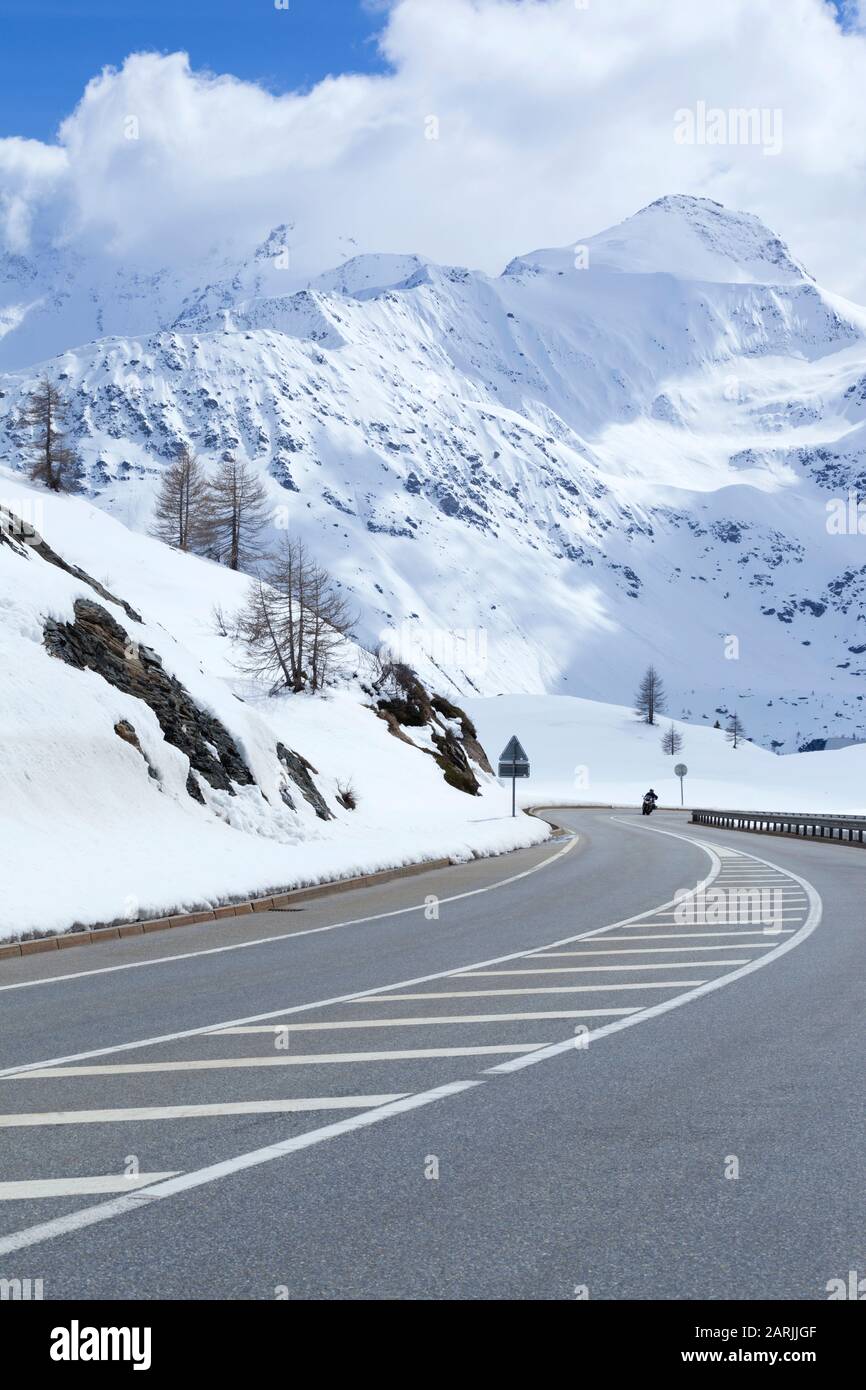 Asphalt road in an alpine valley with mountain peaks covered with fresh snow . Stock Photo