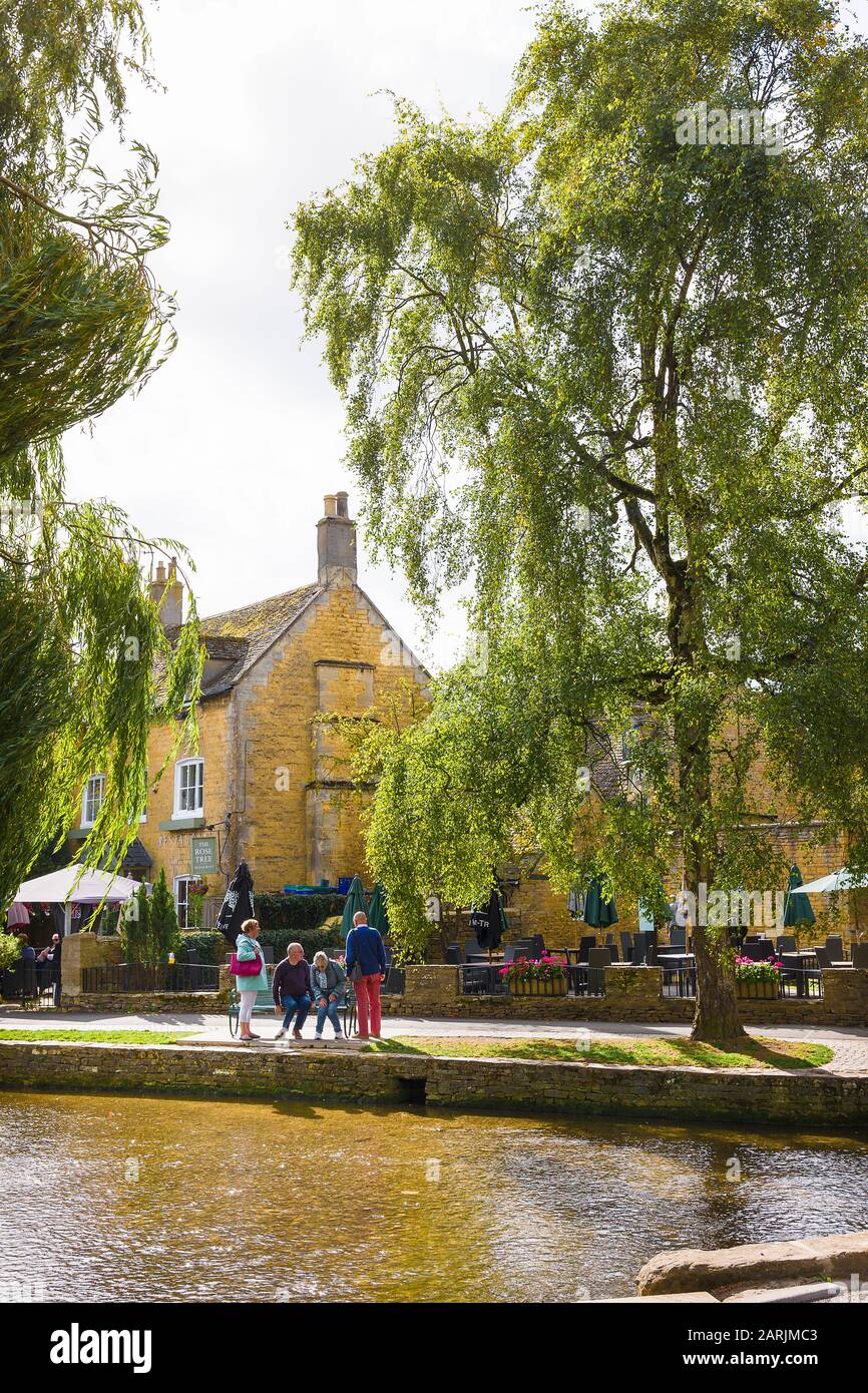 A group of senior tourists beside the shallow River Windrush in Picturesque Bourton on the Water in the English Cotswolds UK Stock Photo