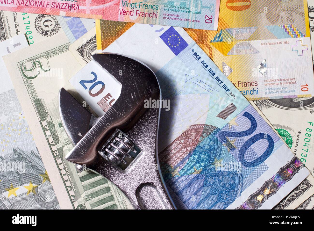 Adjustable wrench on a stack of various Euro, US dollar and Swiss franc banknotes. Stock Photo