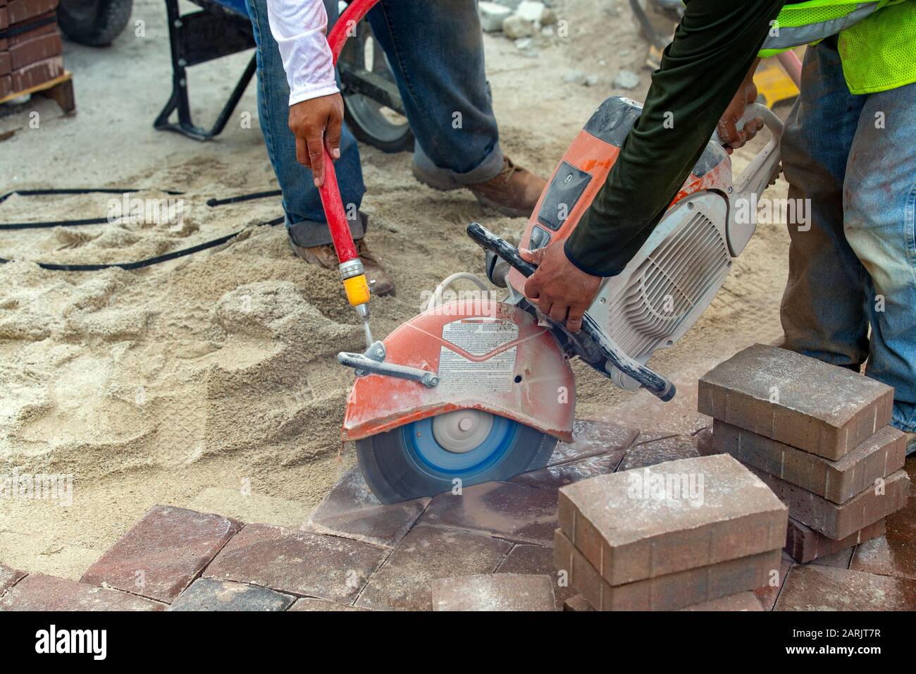 man, laborer cutting and sawing paving bricks in a straight line. Stock Photo