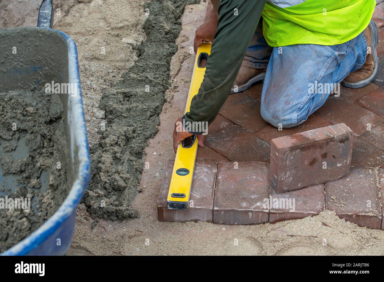 Brick layer or paver measuring and using a level to insure that his laid surface is level in preparation for his concrete laid border to lay bricks on Stock Photo