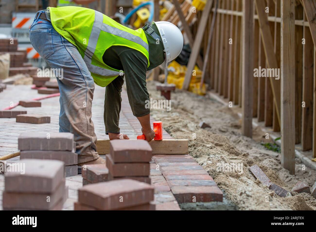 Brick Layer, paver tamping on a piece of wood to adjust the hight of a payed paver brick Stock Photo