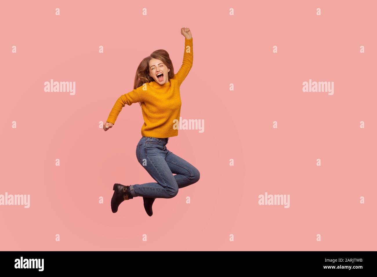 Vivid energetic ginger girl in sweater and denim jumping in air or flying up, shouting Yeah i did it, celebrating victory success, full of enthusiasm. Stock Photo