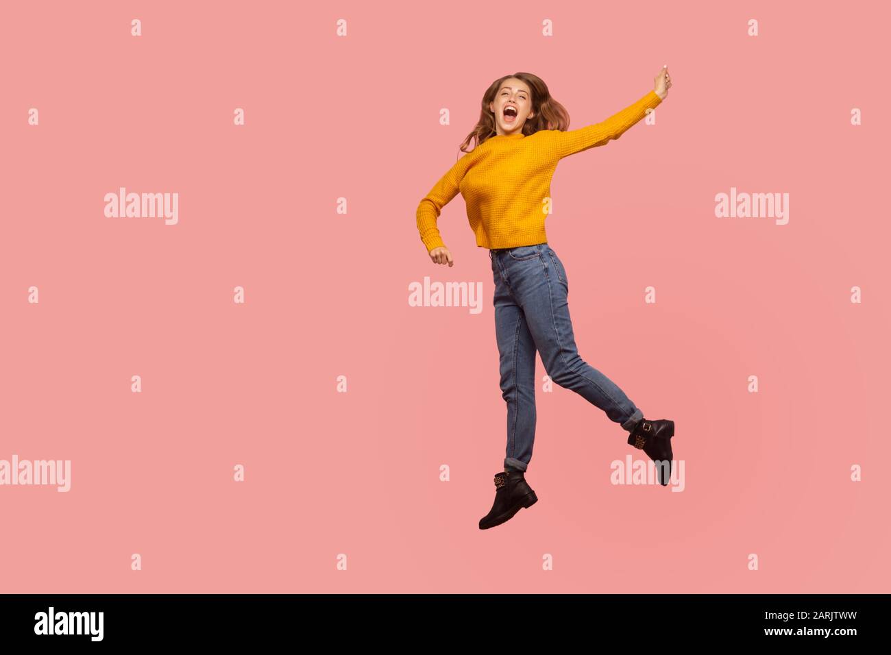 Portrait of lively energetic ginger girl in sweater and denim full of enthusiasm jumping in air or flying up, screaming from happiness. indoor studio Stock Photo