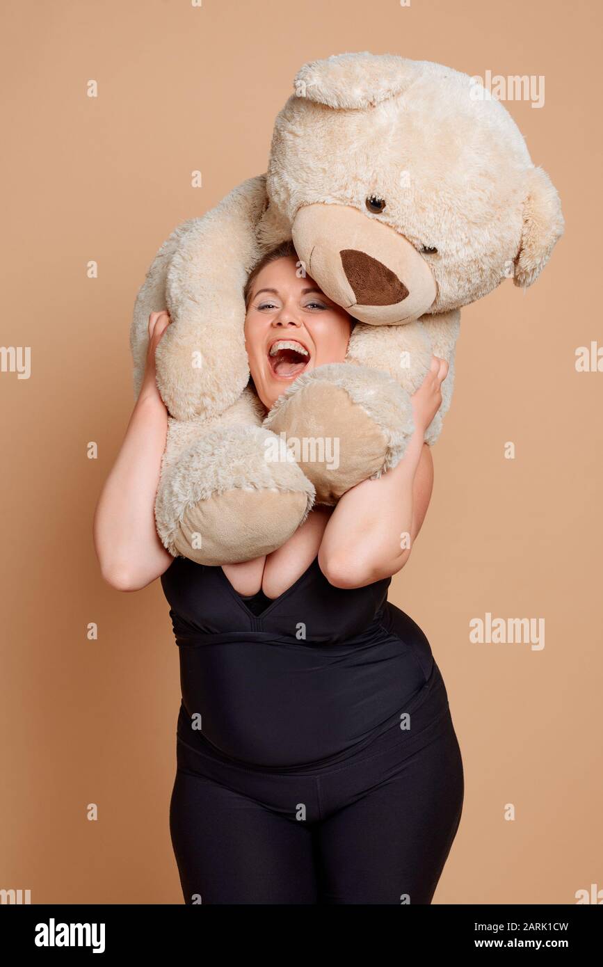 Overweight woman playing with Teddy bear on beige background Stock Photo
