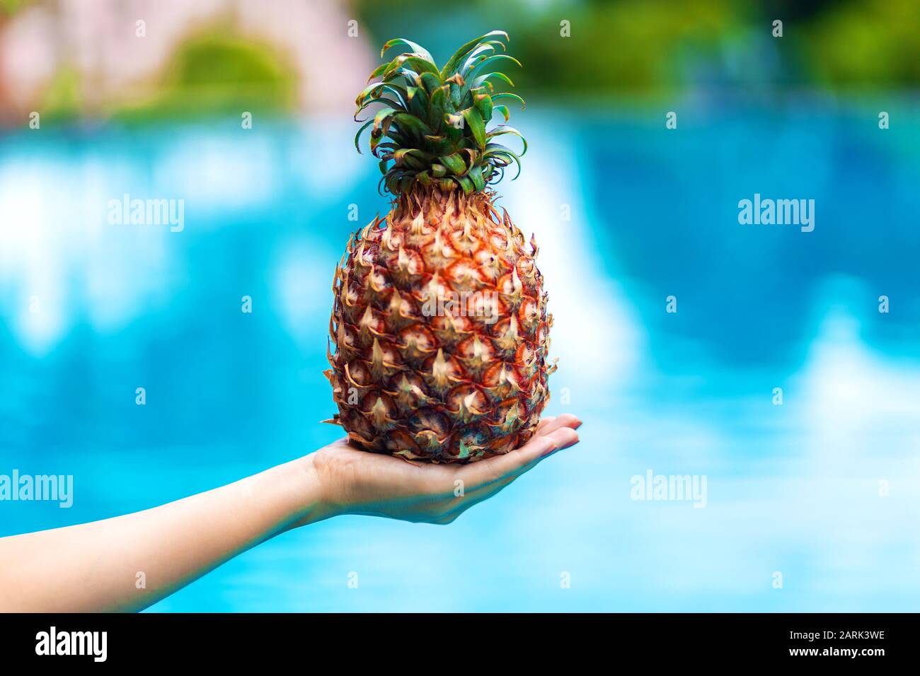 Girl holds ripe pineapple fruit on a background of a pool with blue ...