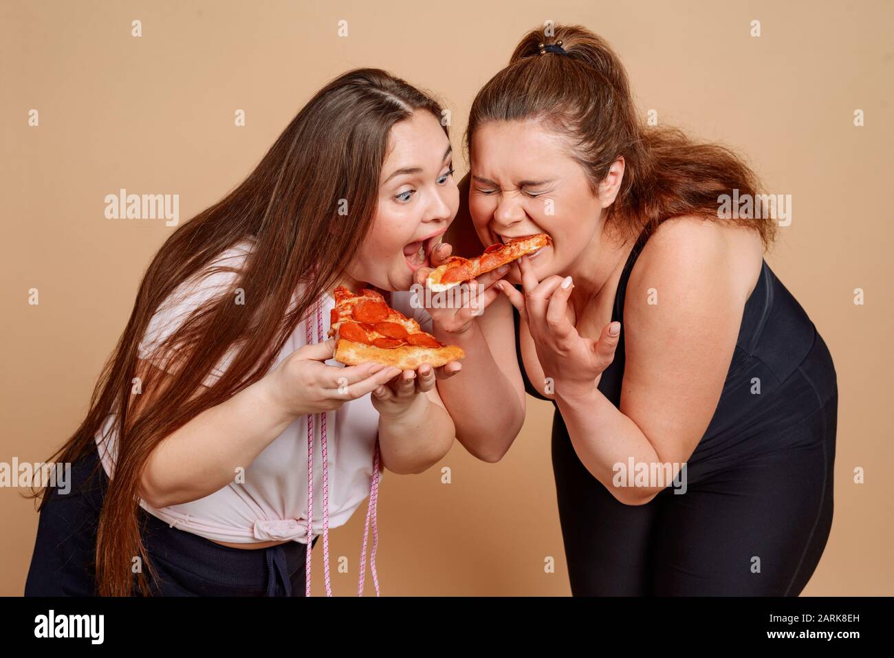 Two girls eating pizza greedily after gym classes Stock Photo
