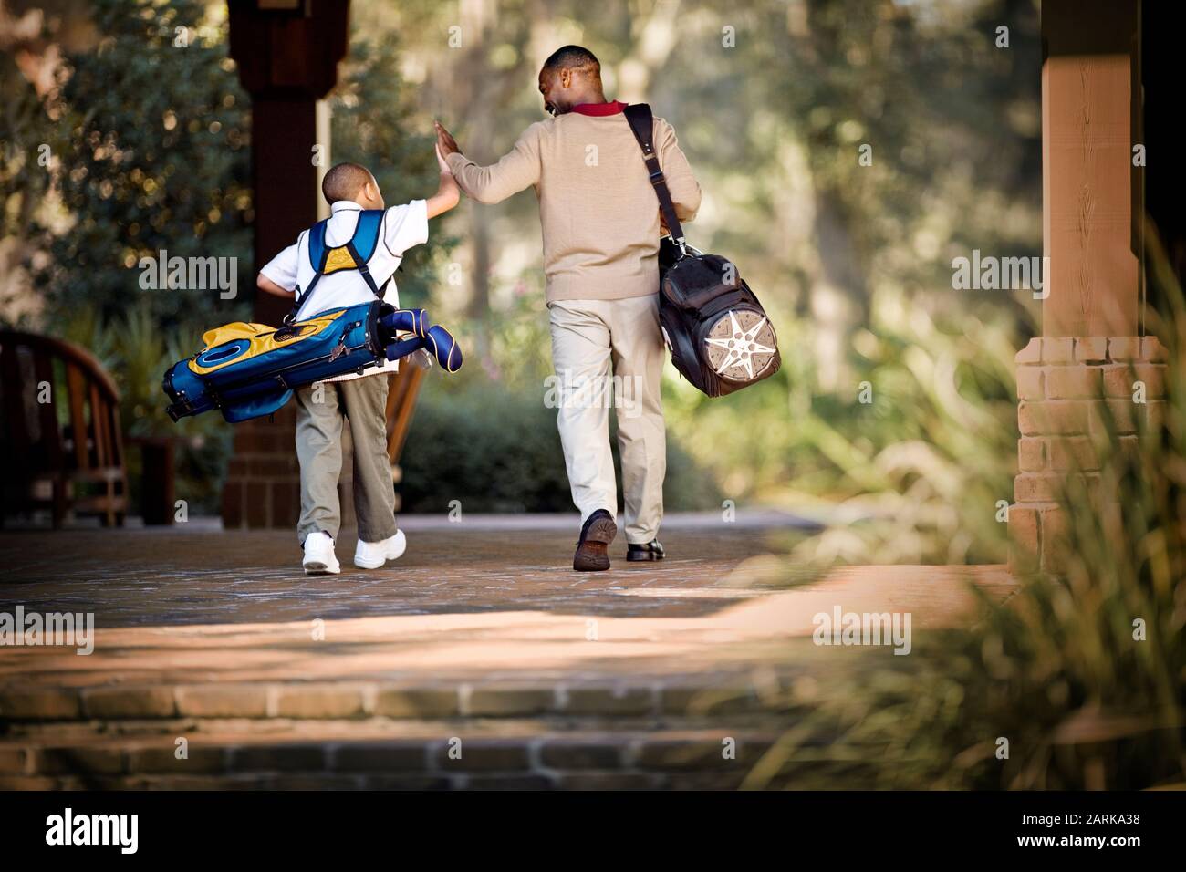 Father and son carrying golf bags and high fiving Stock Photo