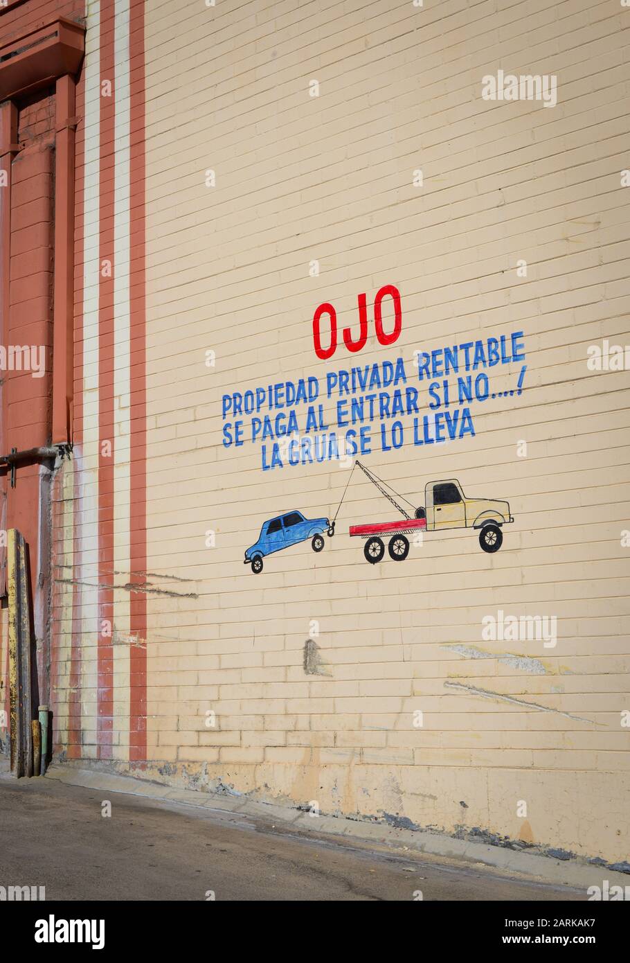 Spanish language stenciled onto old brick wall with childlike drawing and warning to pay to park on private property or car will be be towed by tow tr Stock Photo