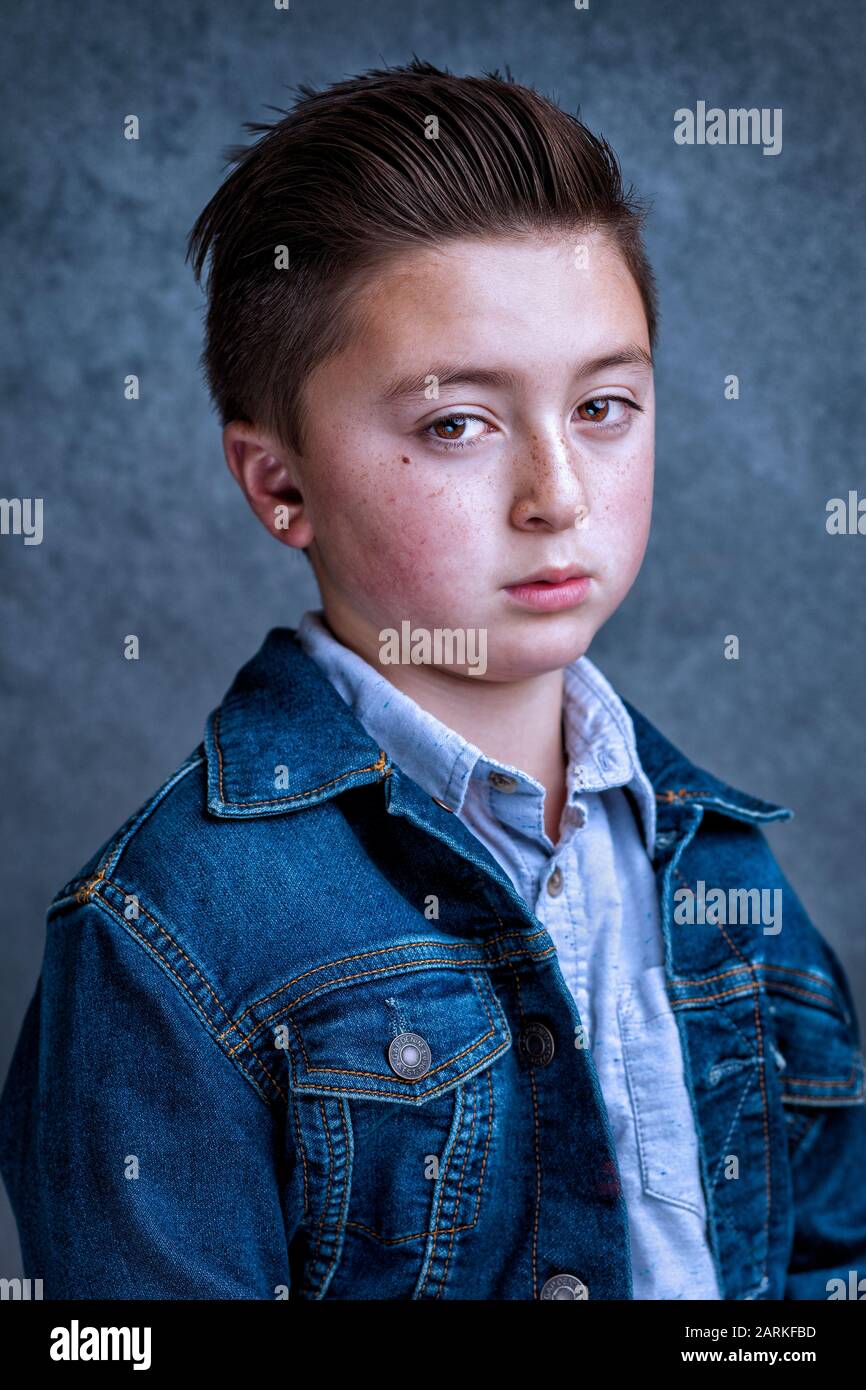 Handsome multi-racial Asian Caucasian little juvenile delinquent boy with an angry frown wearing a blue denim jean jacket with greased styled hair Stock Photo