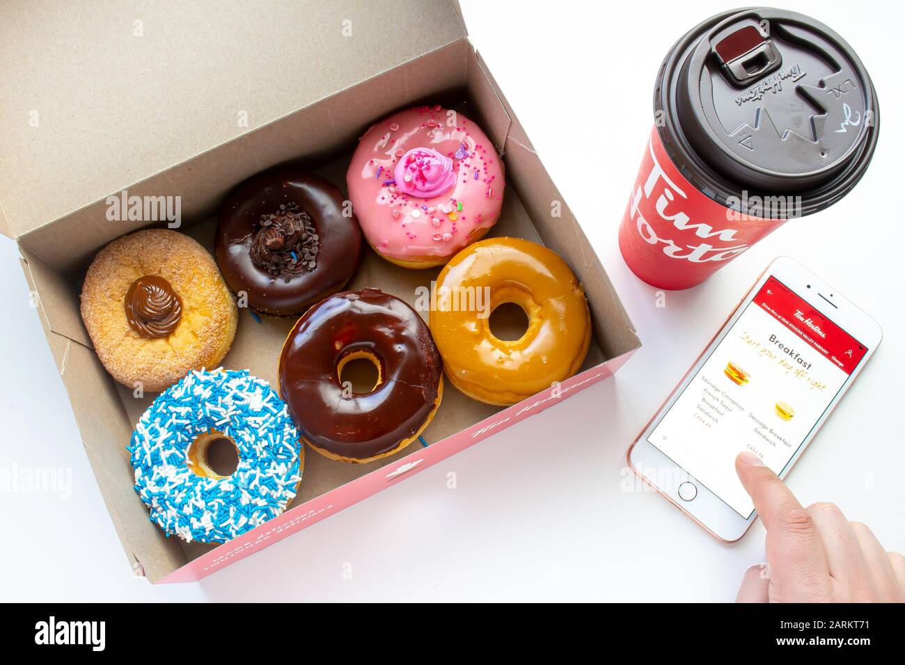 Calgary, Alberta. Canada Jan 27 2020. A person using an iPhone Plus using the Tim Hortons app with a coffee and a open box of donuts on a white backgr Stock Photo
