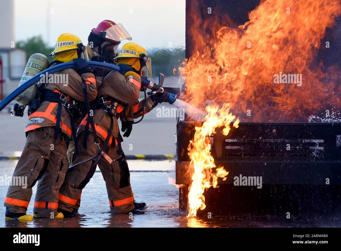 U.S. Air Force Airman Kristina Schneinder, 312th Training Squadron student, leads Airman Emalie Lemons, 312th TRS student, in a textbook style approach to a mock vehicle fire outside the Louis F. Garland Department of Defense Fire Academy on Goodfellow Air Force Base, Texas, July 11, 2019.  Schneinder and Lemons were trained in the classroom how to approach a live fire and what angle to spray the water hose for hood and undercarriage fires before their hands on experience. (U.S. Air Force Photo by Airman 1st Class Abbey Rieves/Released) Stock Photo