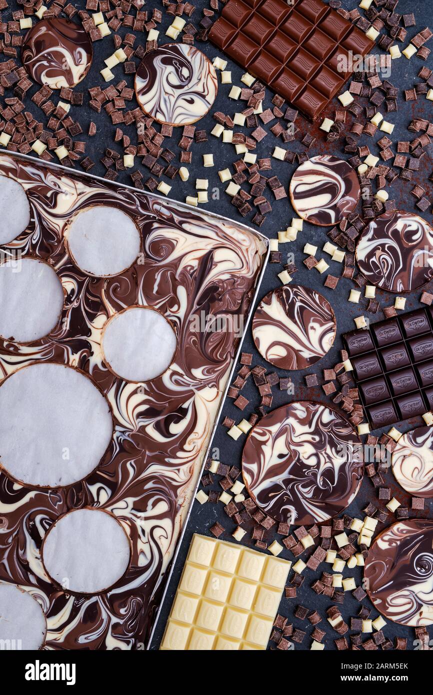 Marbled chocolate discs cut out from a tray with chocolate bars and chunks on a slate background Stock Photo