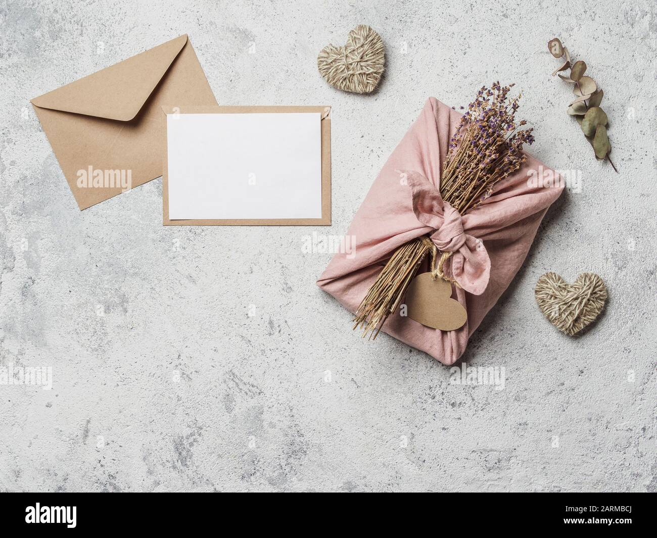 Zero waste Valentine's Day concept and mock up. Eco-friendly gift cloth wrapping in Furoshiki style, craft paper envelope, empty gift or greetings card, copy space Stock Photo