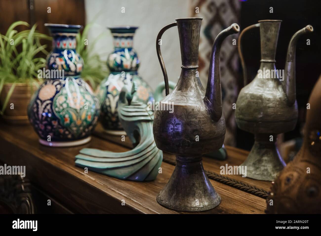 An ancient copper decanter and an ornate clay jug stand on a shelf. Stock Photo