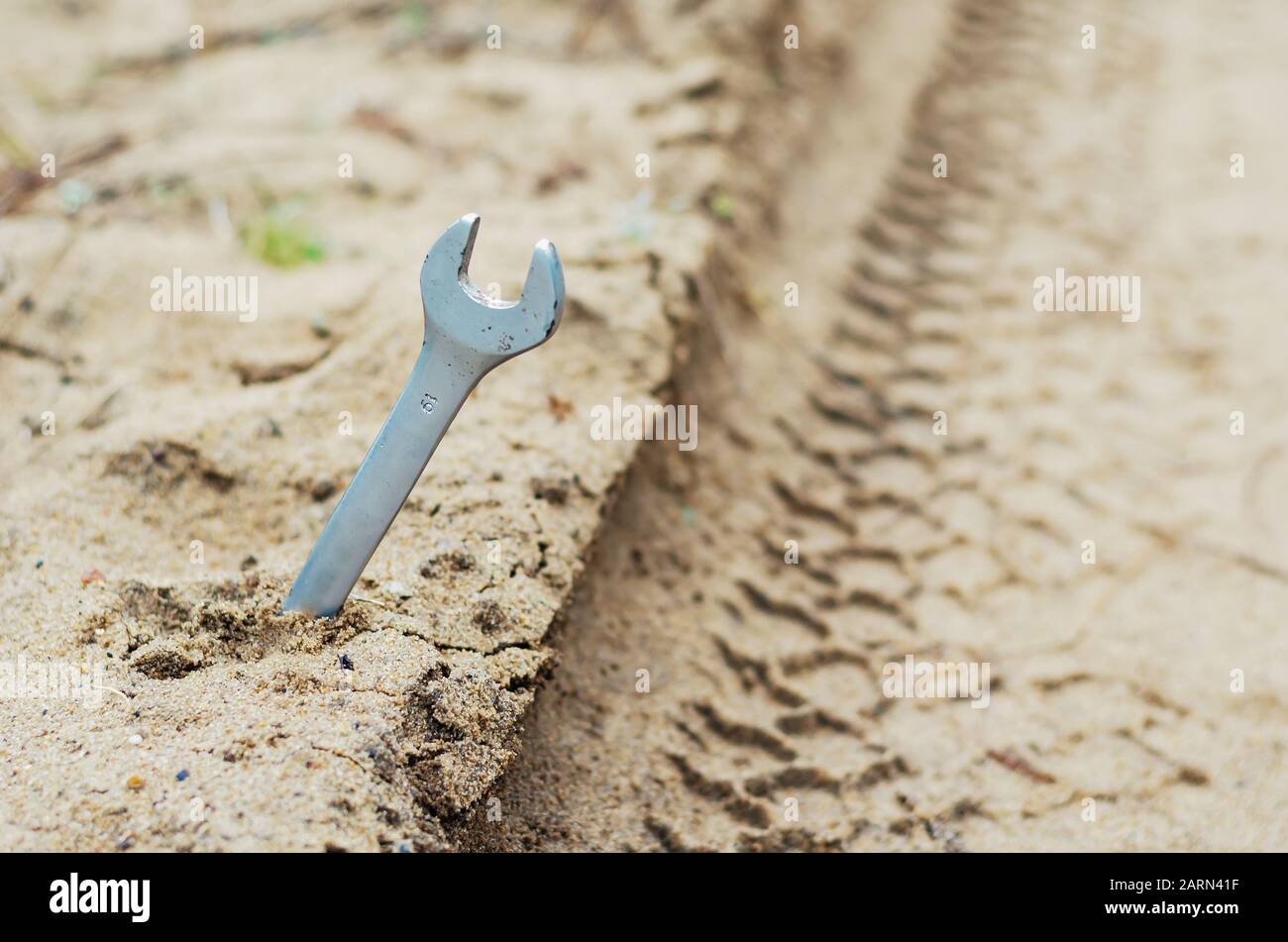 A metal wrench stops a passing car on the edge of a sandy road. Wrench