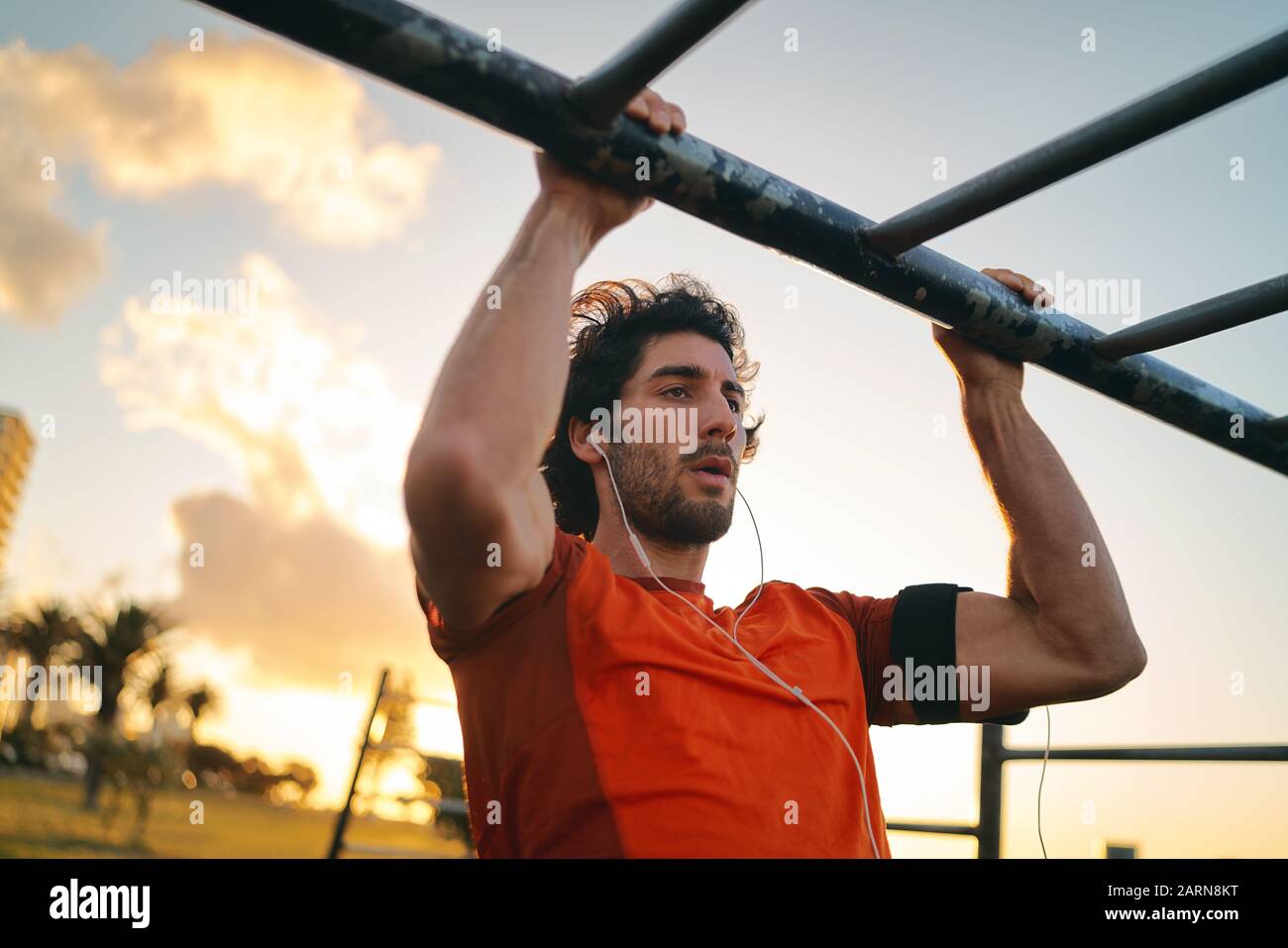 Healthy fitness young man listening to music on earphones doing pull-ups in outdoor gym park - man doing chin-ups Stock Photo