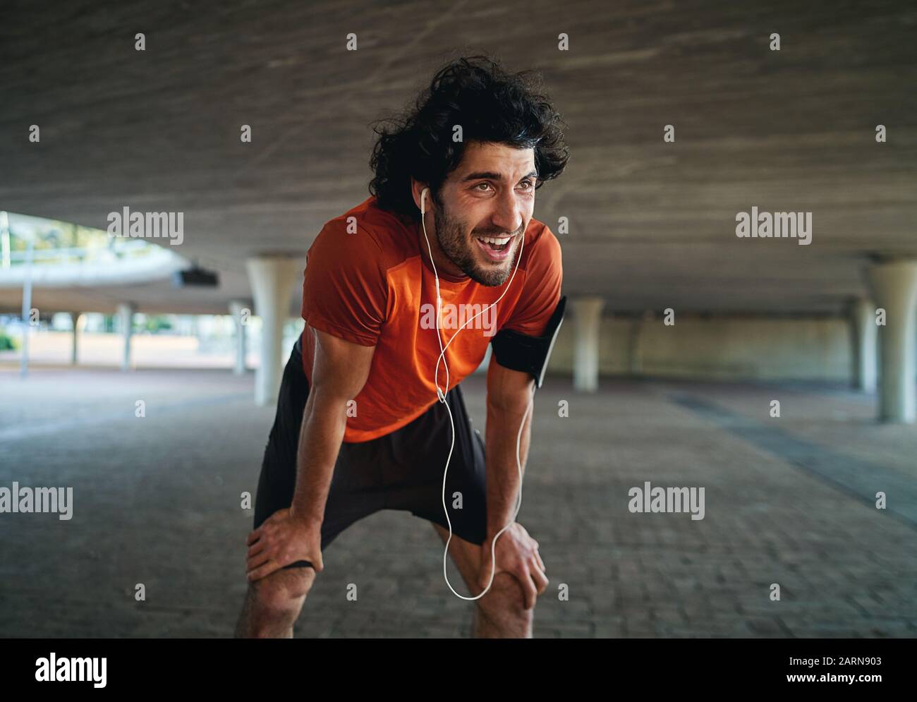Portrait of sweaty and tired young male fit person taking a break after jogging in city street under the bridge Stock Photo