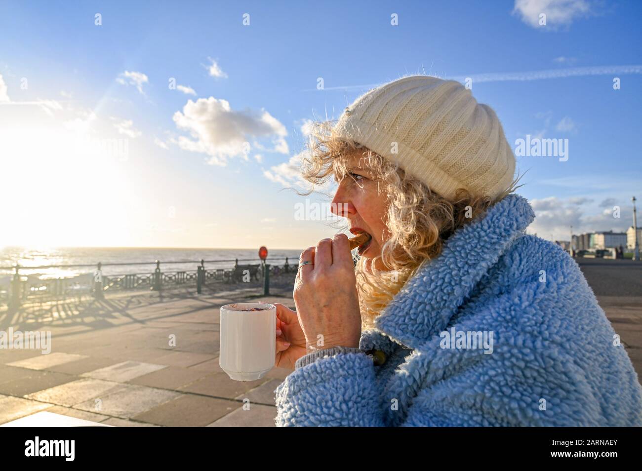 Mature middle aged woman enjoying a cup of coffee and cookie at a Brighton seafront cafe on winter sunny day Stock Photo