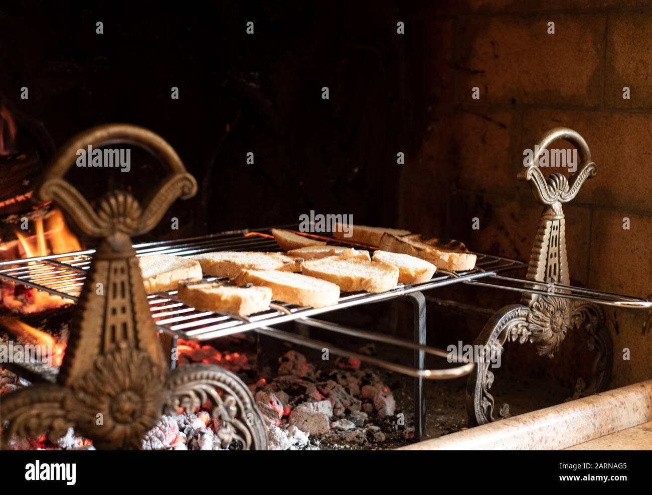 Assorted sliced bread toasting on a metal rack over hot coals and fire with flames in a fireplace indoors with copy space above Stock Photo