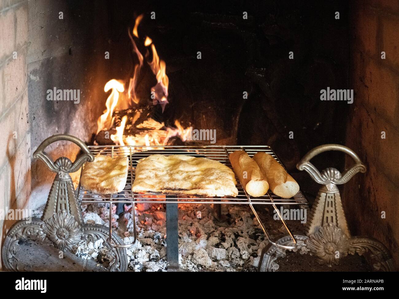 Bread heating on a rack over hot coals in a brick fireplace with burning fire in close up Stock Photo