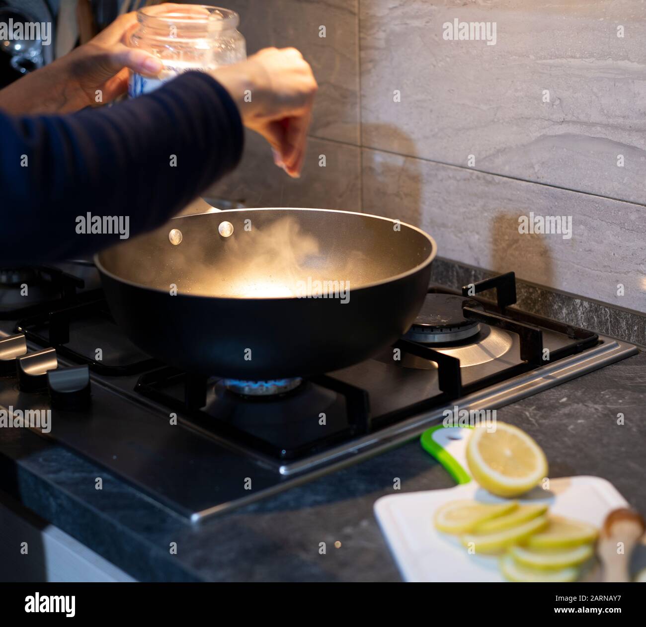 Woman cooking over a hot frying pan on a gas cooker in a kitchen adding
