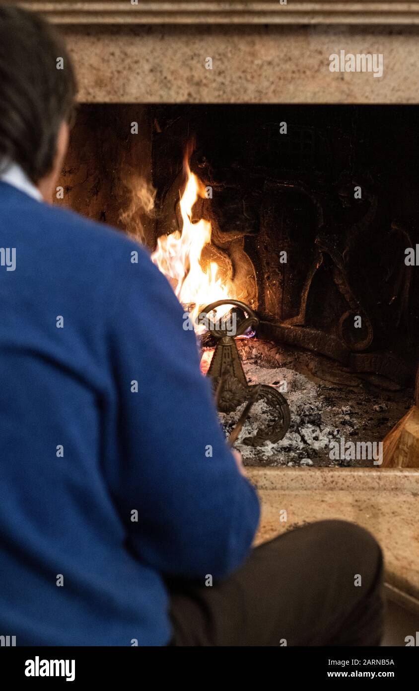 Rear view of a man sitting in front of a hot fire burning in a brick fireplace indoors in winter Stock Photo