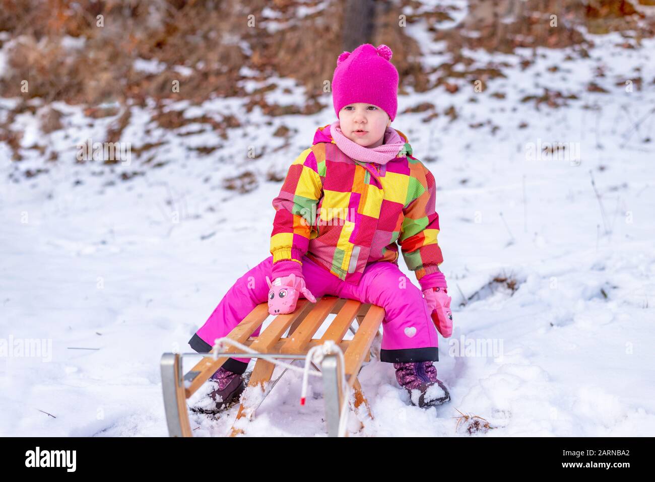 Cute girl on sled dressed in winter clothes. Concept of a game of snow that improves the health of children in the winter Stock Photo
