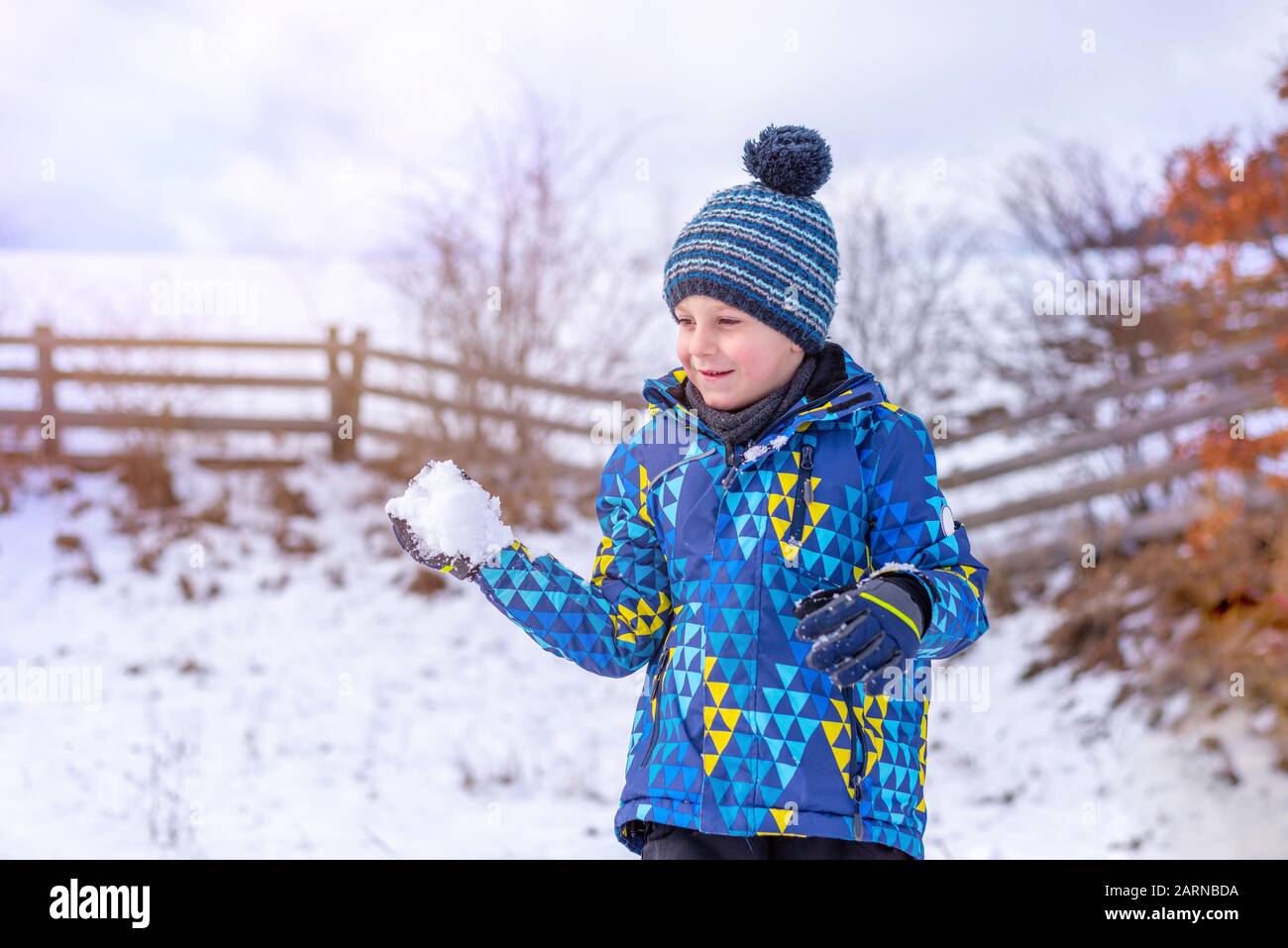 Boy holds a snowball in his hand and tries to throw it. Concept of child play on snow and the development of immunity Stock Photo